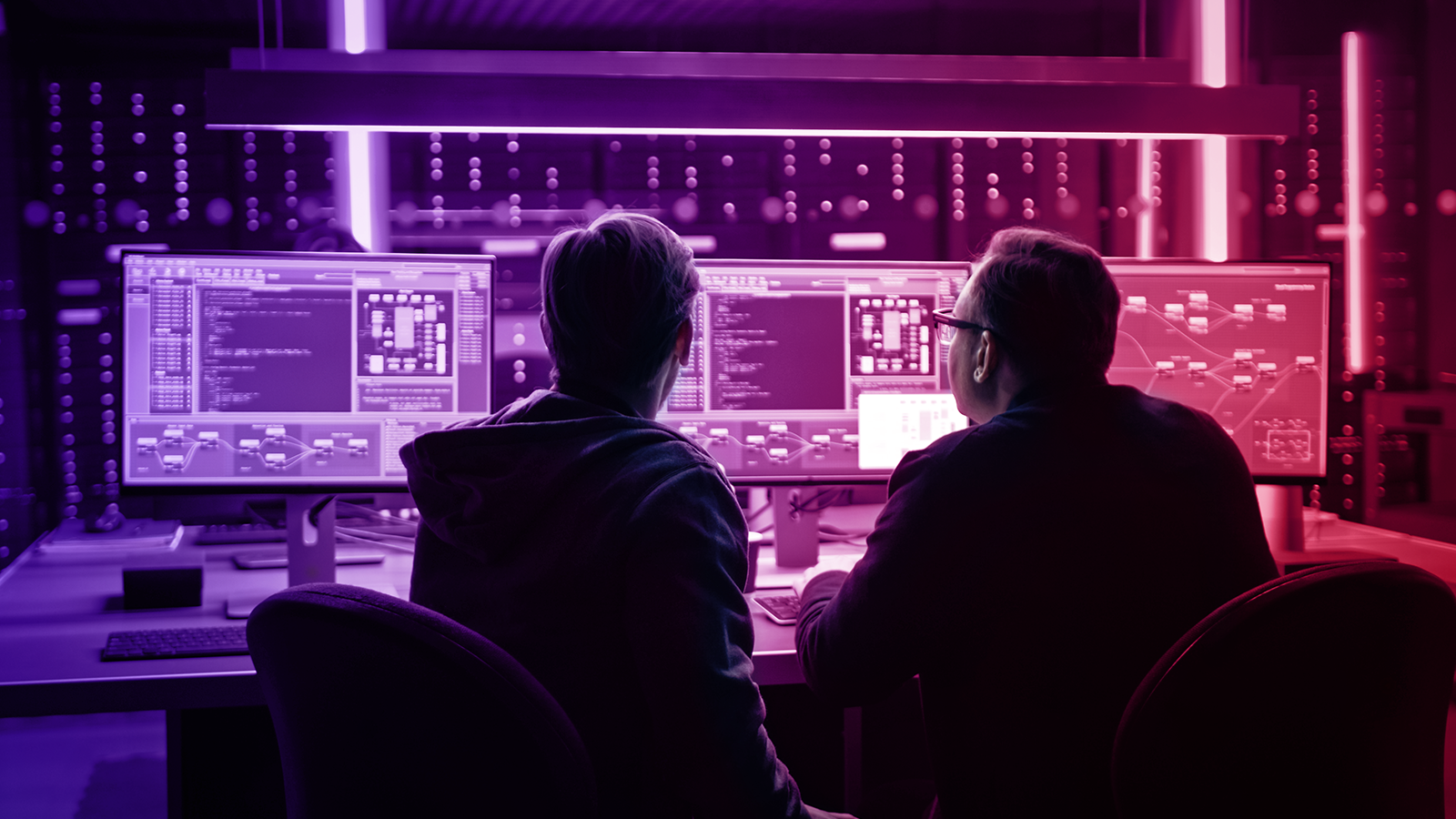 Two people working at multiple monitors displaying code and network diagrams