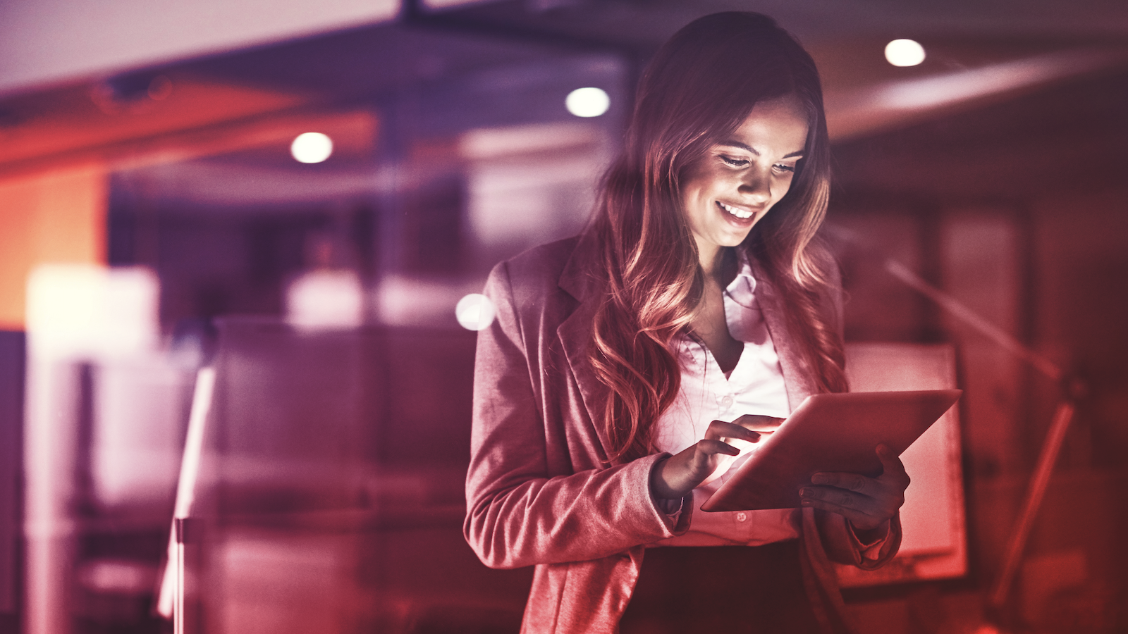 Woman stands by window and uses tablet in dim setting