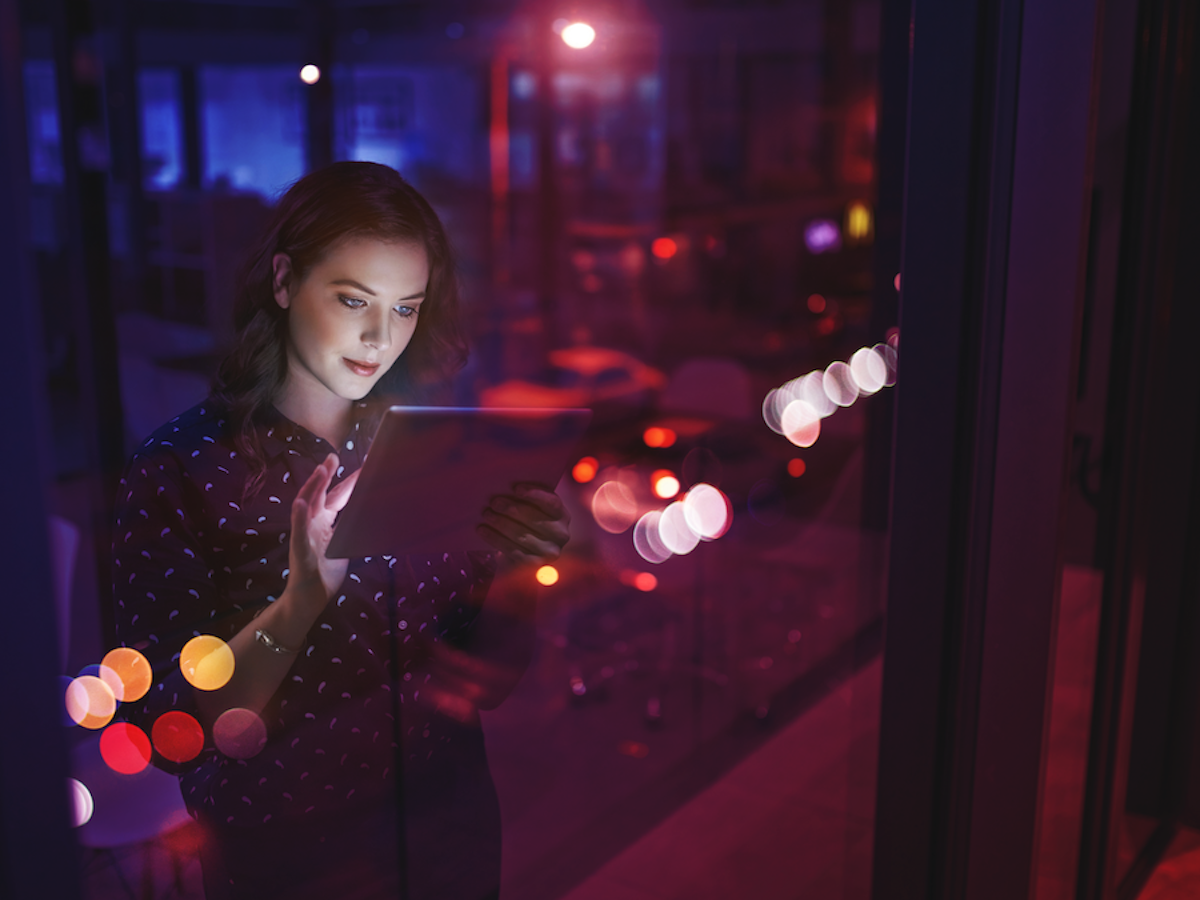 Woman stands by window and uses tablet in dim setting